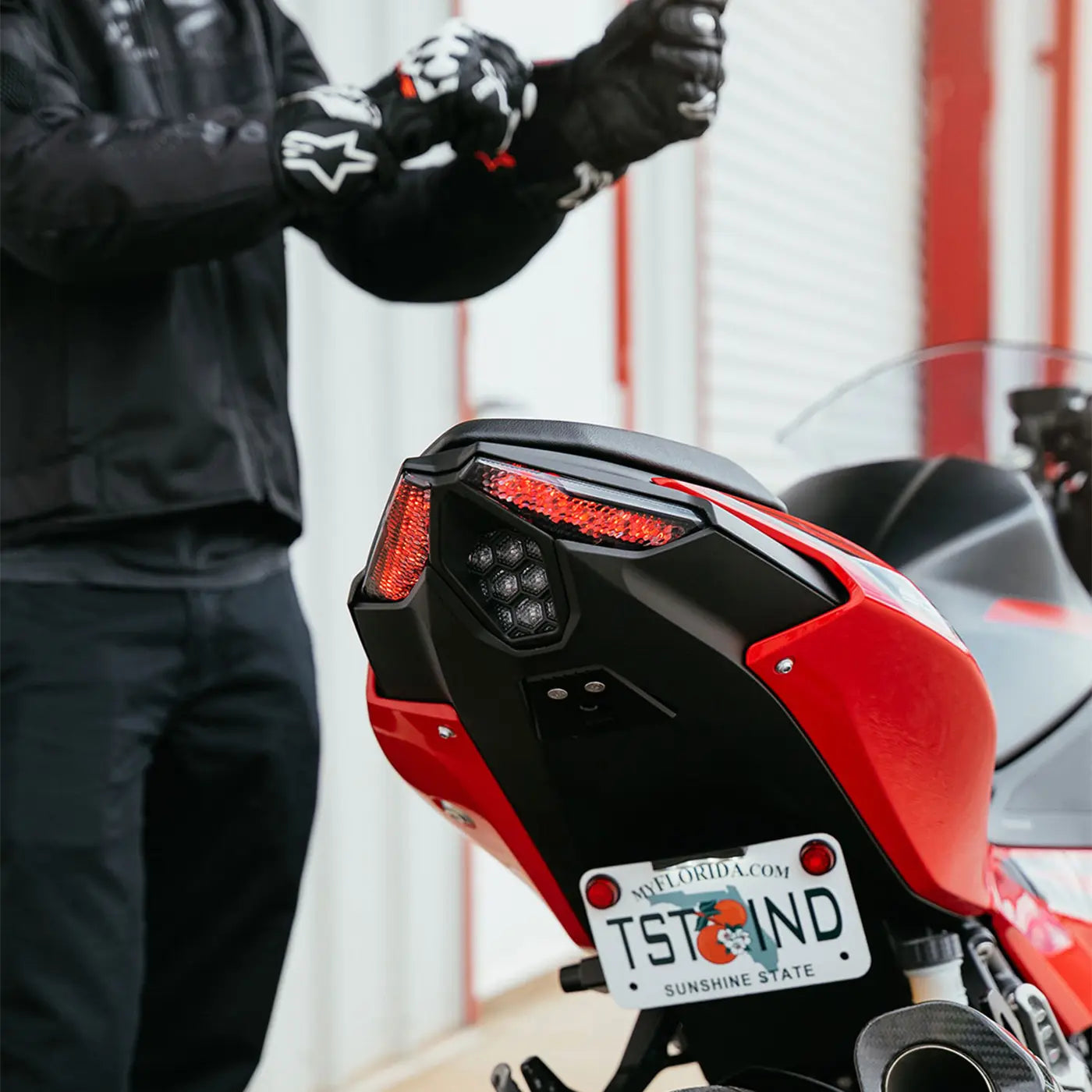 Close up image of the tail section of the 2025 Kawasaki Ninja 500 with the TST Industries LED Integrated Tail Light installed while a rider puts motorcycle riding gloves on in the background.
